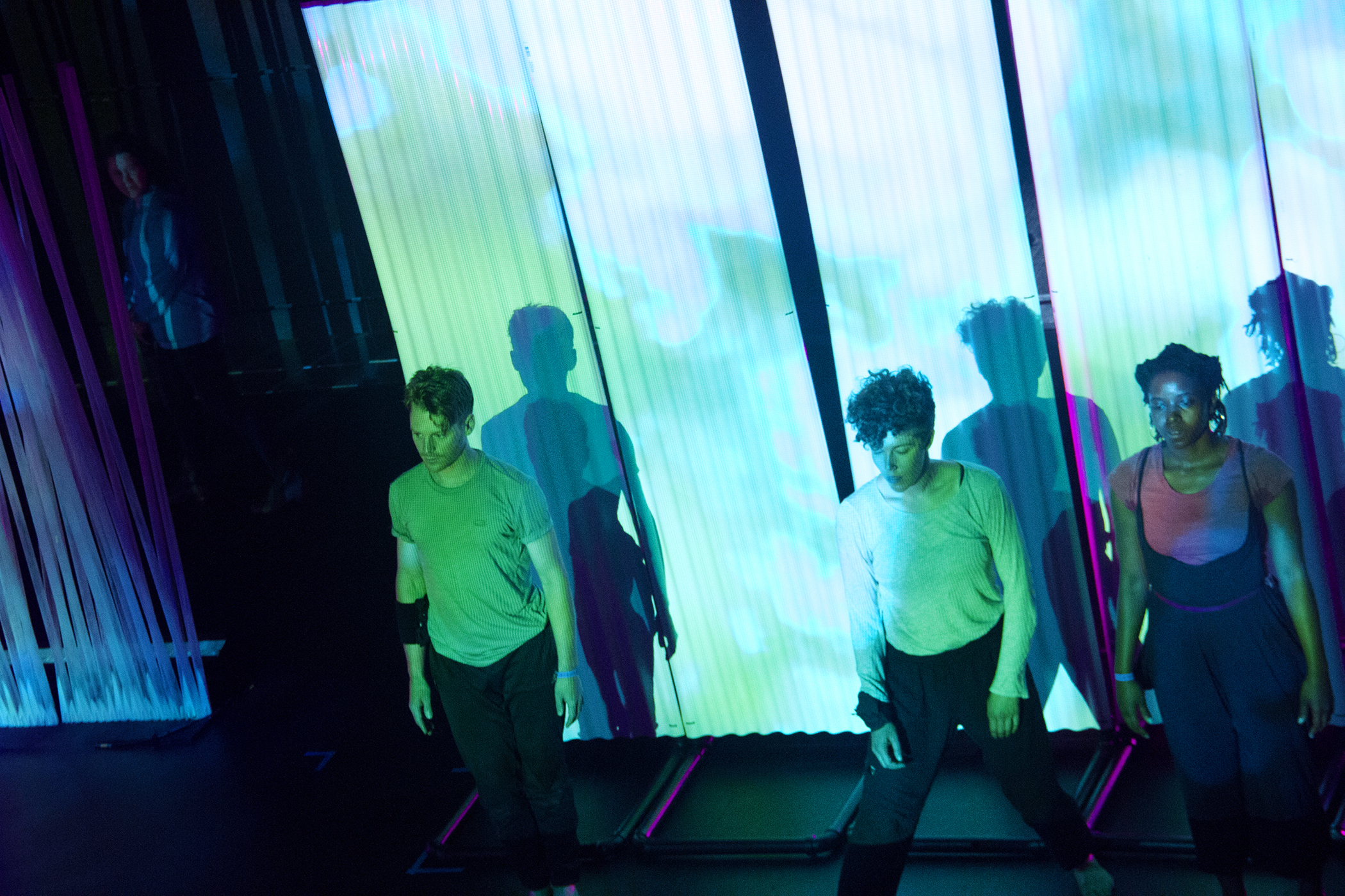 Performers in a space illuminated by cyan and green projections.